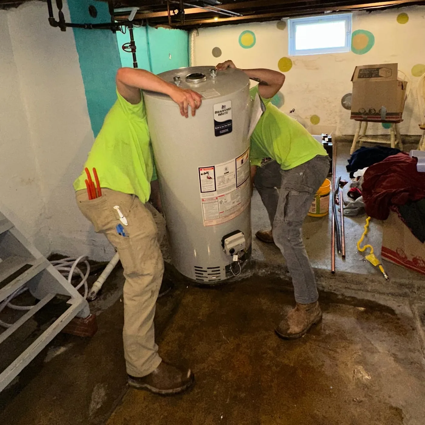 Two Pioneer technicians moving a residential water heater into a basement utility space