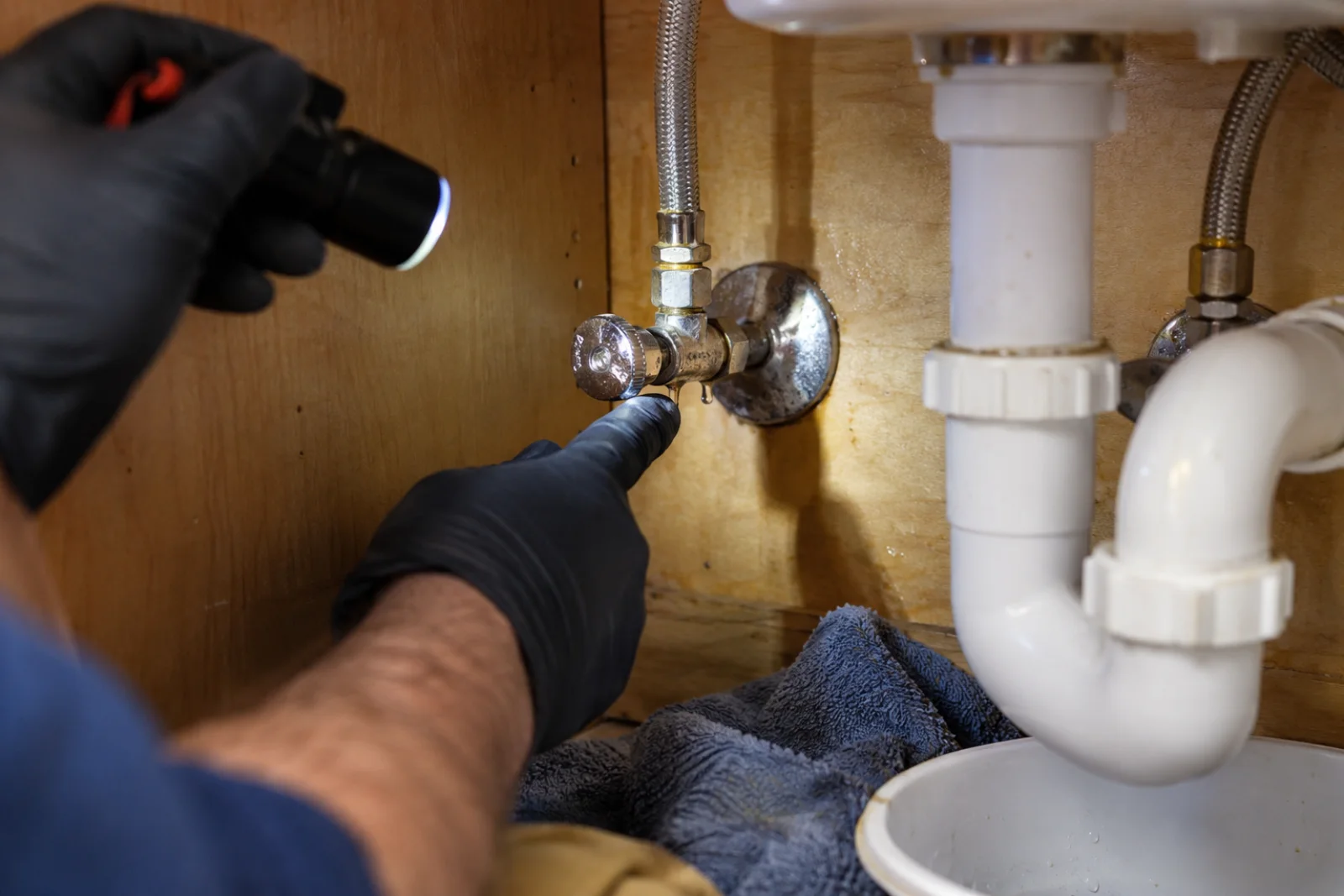 Plumber using an inspection light to trace a small drip at an under-sink supply connection